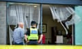 A man and a police officer stand in front of a completely destroying glass wall of a Holiday Express