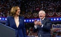 A woman and a man laugh while standing in front of a large crowd at a political rally