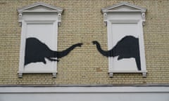 Black spraypainted elephant heads face each other from two white-painted blocked-out windows, with their trunks reaching out towards each other