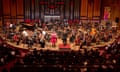 A female African soloist sings in front of a symphony orchestra in a concert hall