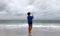 person stand on beach shore holds phone up