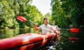 A young couple are smiling while paddling together on the river in a kayak.