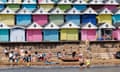 Families on the beach in front of rows of beach huts in Walton-On-The-Naze, Essex.