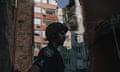 Man in uniform and protective helmet in shadow with bomb-damaged building in sunlight in background