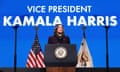 A woman wearing a dark purple blazer speaks at a podium with a blue background reading 'Vice President Kamala Harris.'